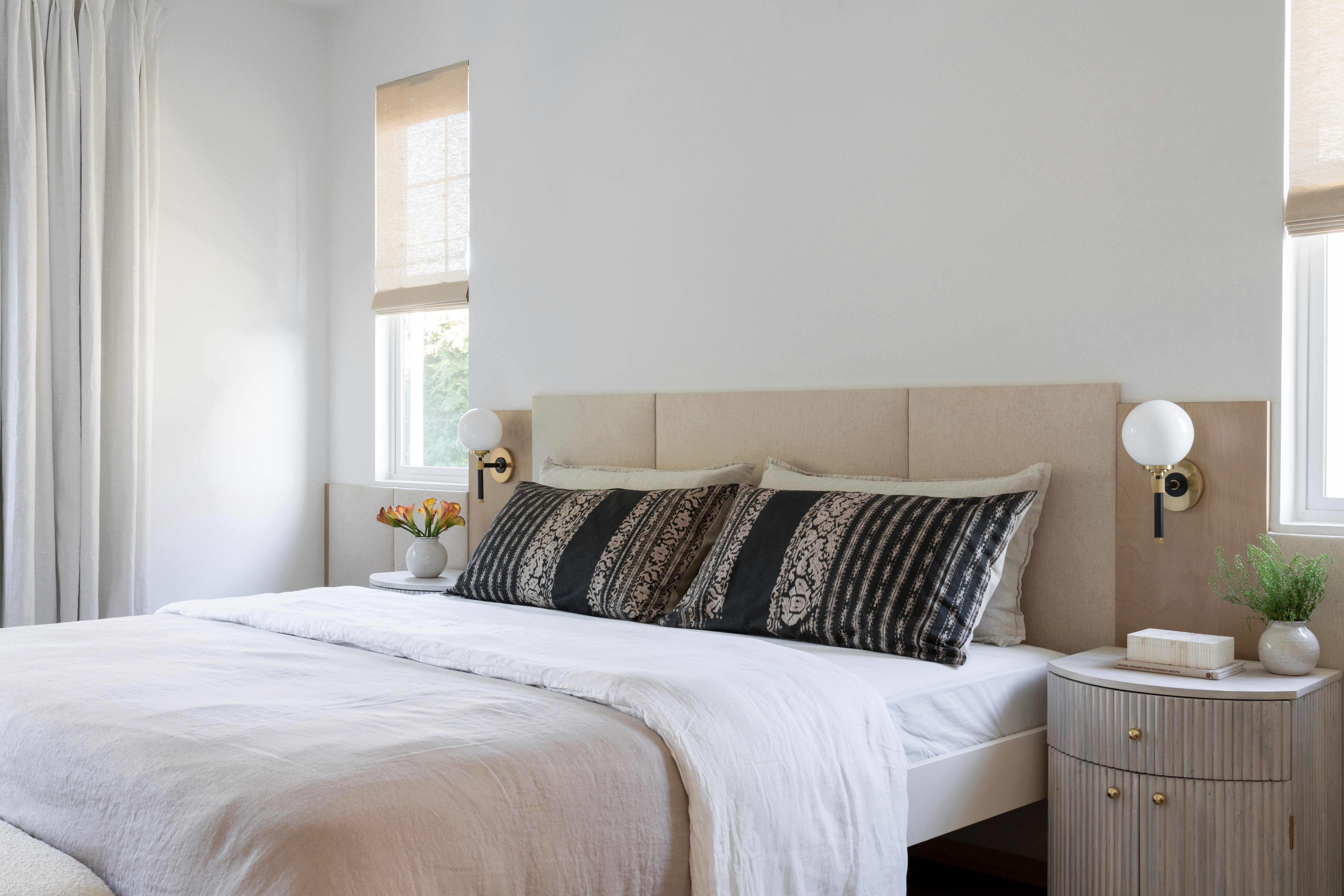 Airy bedroom with linen bedding, paneled headboard, and curved wood side table with brass finishes by Jubilee Interiors in Arcadia, California