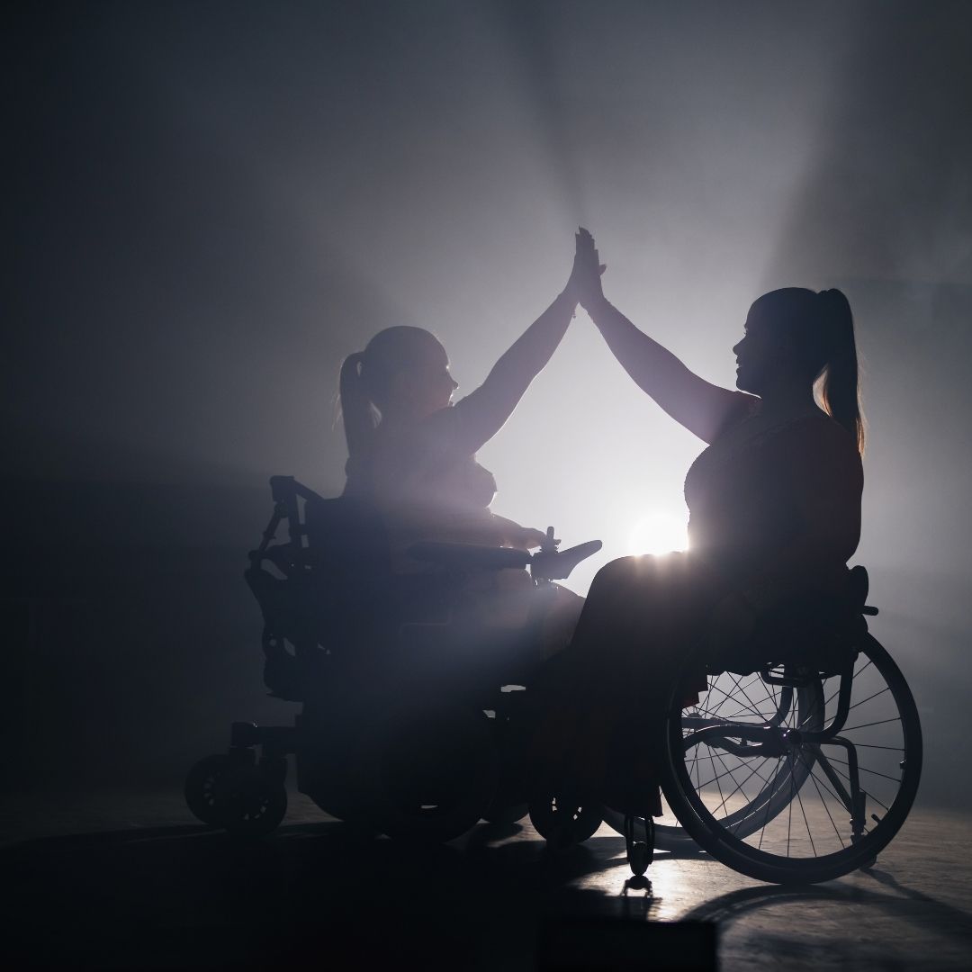 Two female wheelchair users hi-fiving each other
