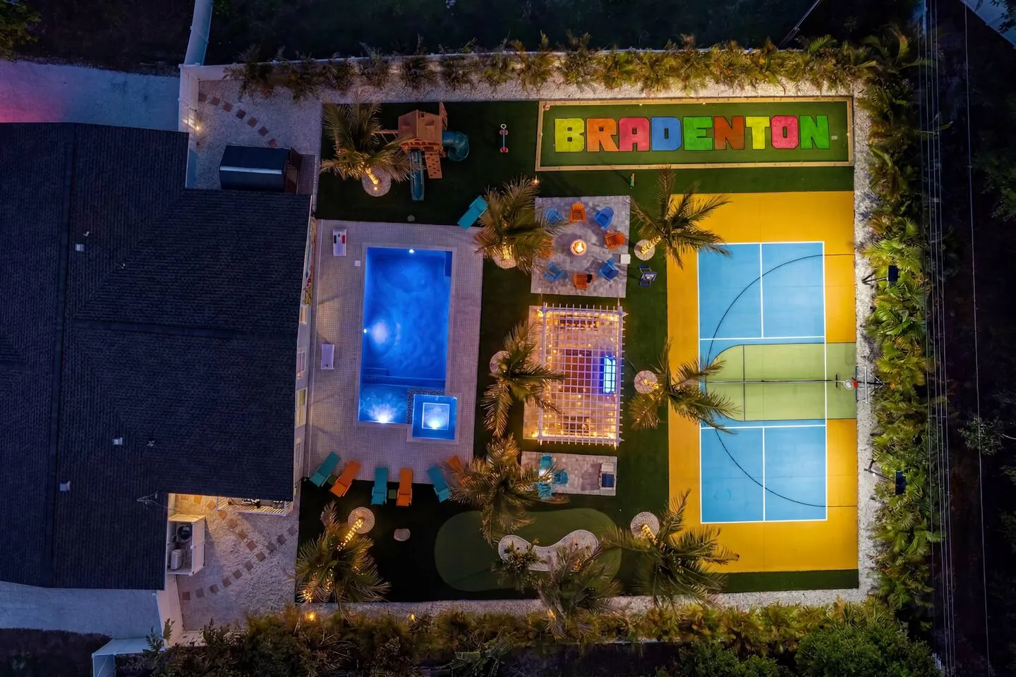 Night aerial with lit court with “BRADENTON” letters and pool at Private Backyard Resort, Bradenton, Florida