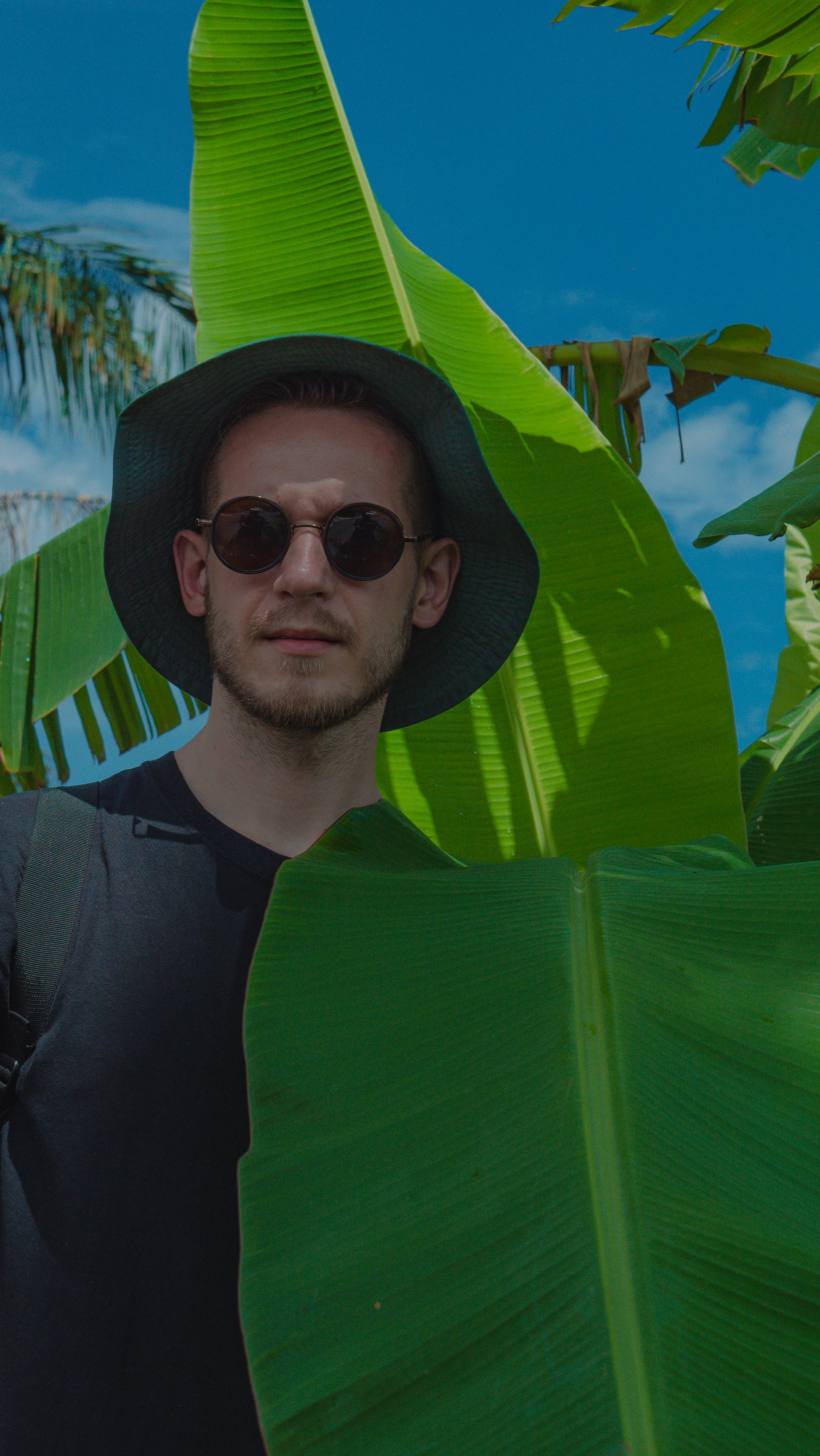 Man in hat and sunglasses among banana leaves