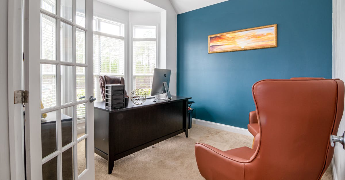 Bright office room with blue accent wall, featuring leather chair and desk in natural light.