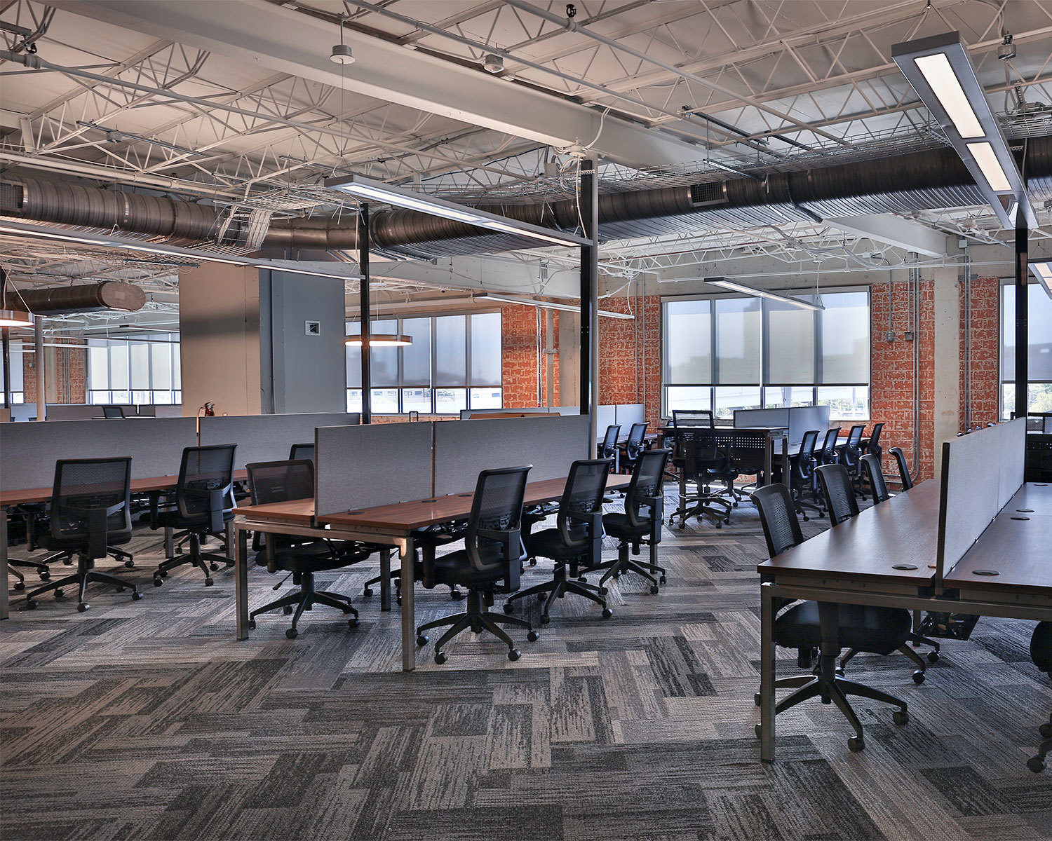 Modern open-plan office featuring ergonomic mesh chairs and long wood-finish benching workstations with privacy screens.