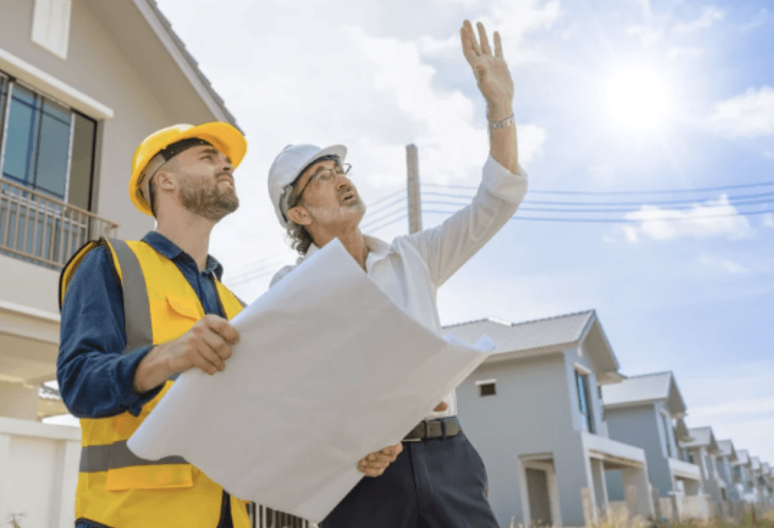 Two women in hard hats review blueprints indoors.