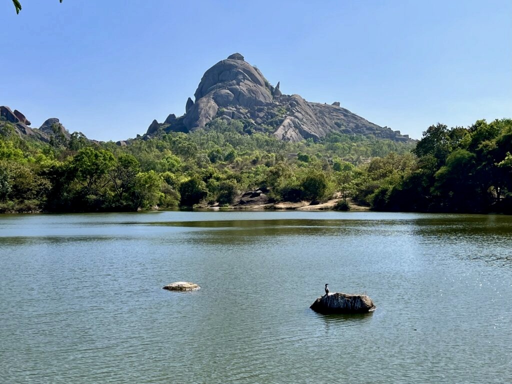 Chandravalli kere and the hill beyond it. A lone bird is resting on a stone in the middle of the lake.