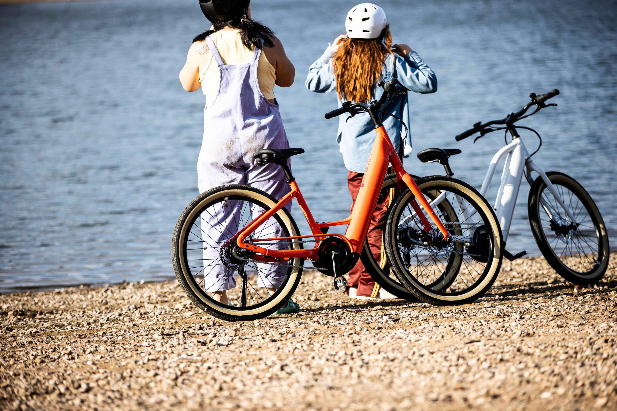 Two cyclists standing with their bikes on a pebble beach, showcasing cycling lifestyle photography, outdoor adventure, community and creative brand campaign storytelling.