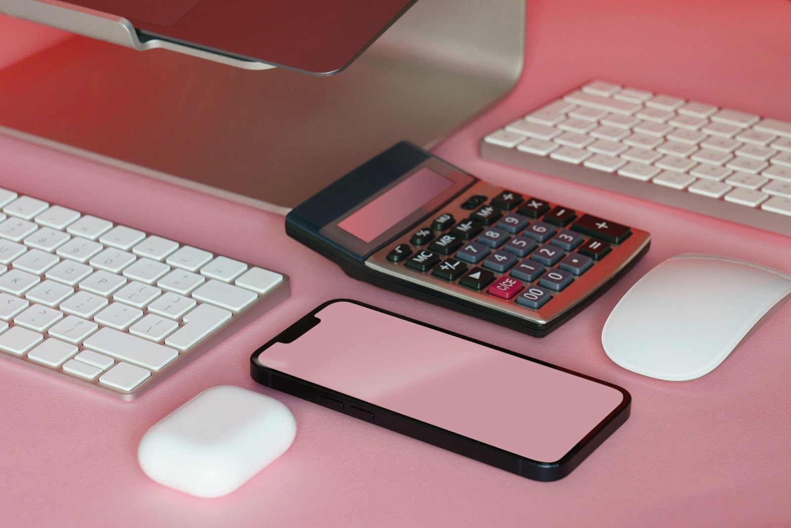 A phone, calculator, keyboard, mouse, and airpods on a pink desk