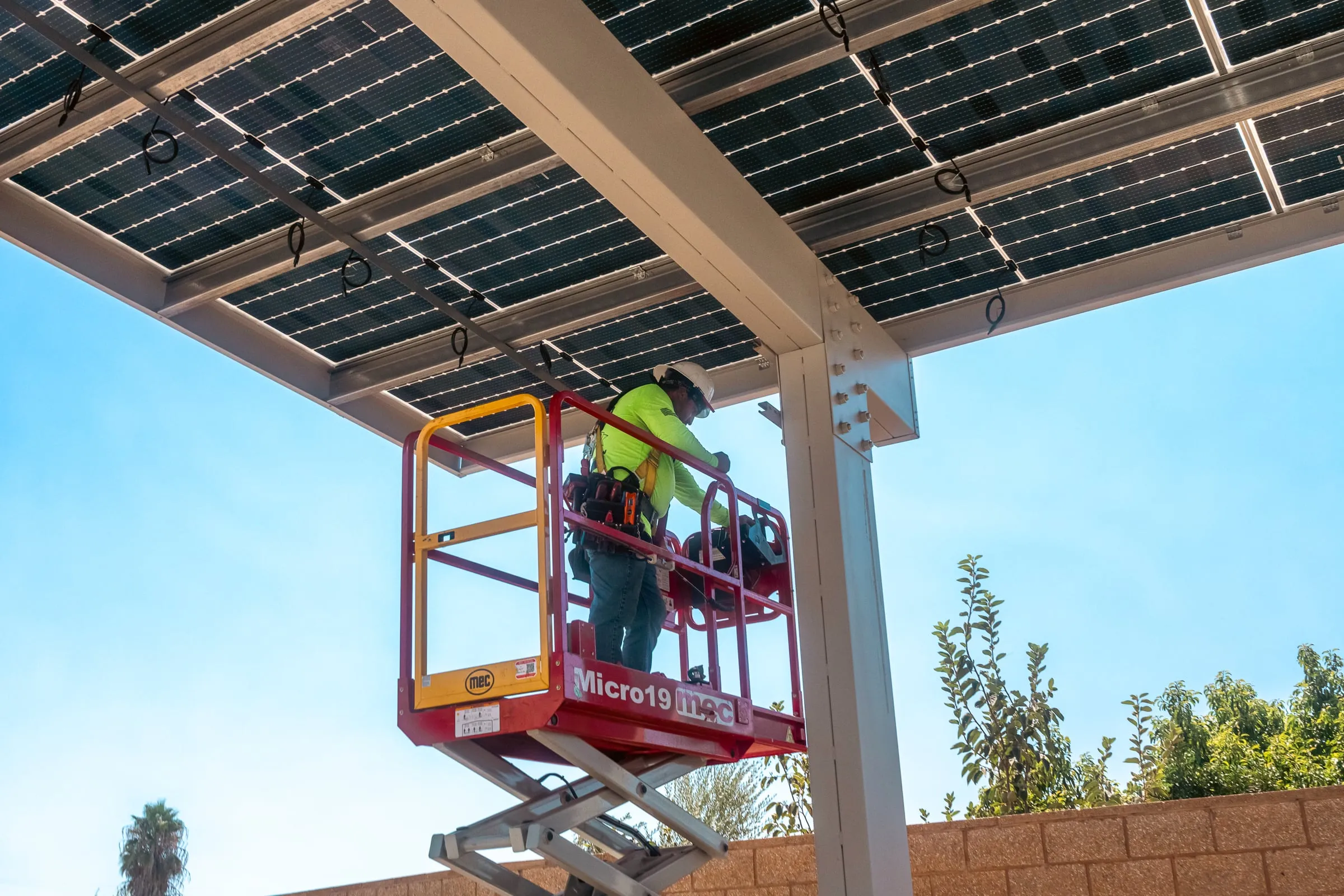 An installer on a scissor lift working underneath a newly built solar carport canopy
