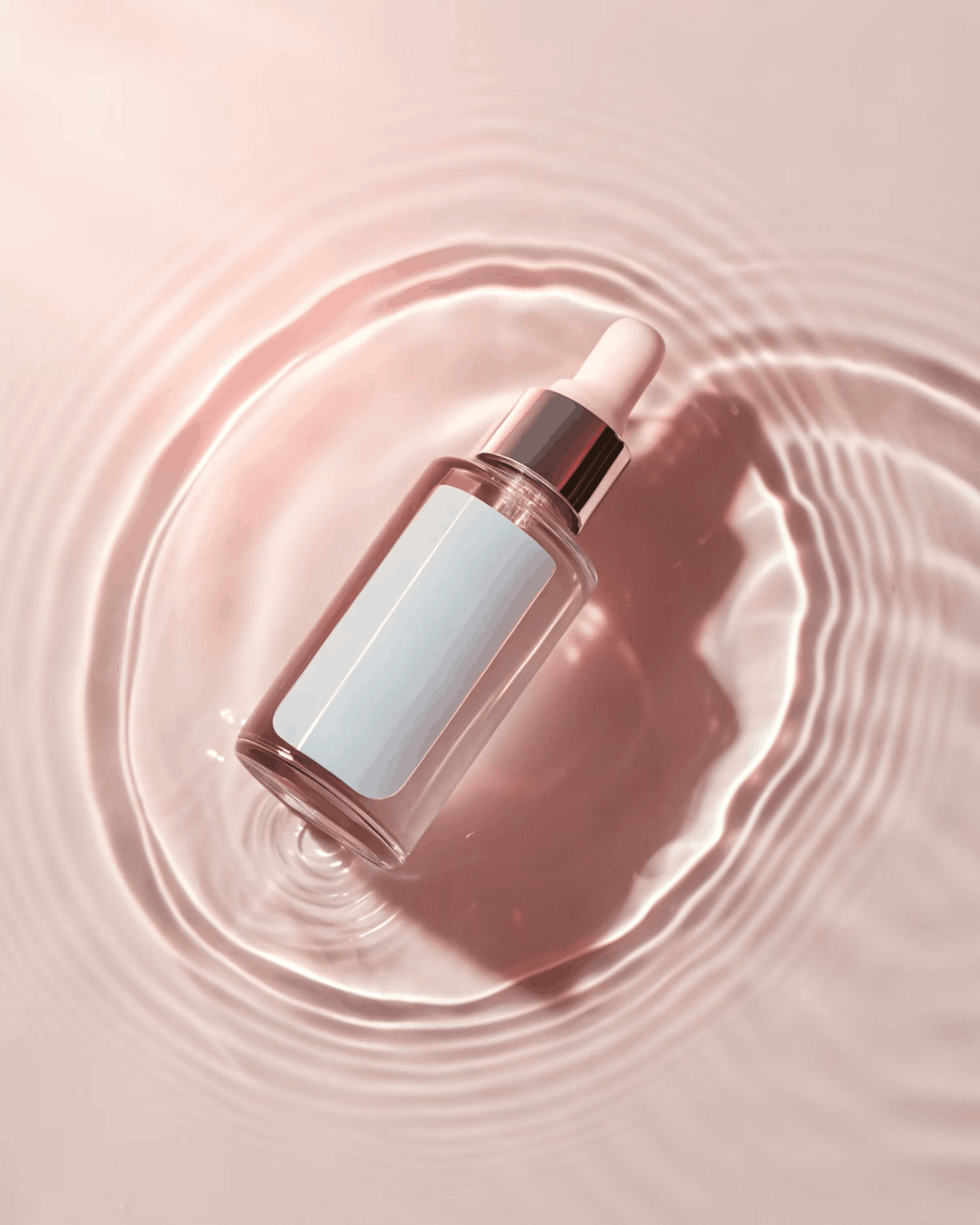 Clear cosmetic dropper bottle in rippled water on a pink surface.