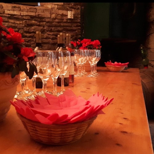 木製桌子上擺放著空的酒杯、酒瓶、紅色花朵的盆栽，以及裝滿紅色餐巾的籃子，營造出一個舒適的環境。