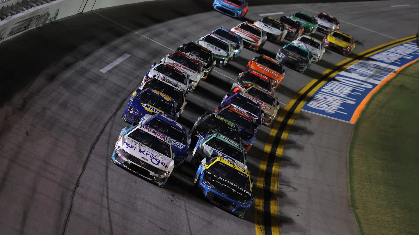 NASCAR Cup Series cars drive in formation under bright lights at Daytona International Speedway during a night race.