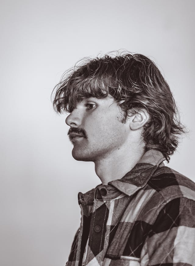 A black-and-white profile of a young man with a mustache in a plaid shirt
