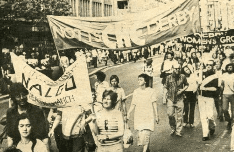 A black and white image of women and men marching with banners reading 'Notts CHE Derby'. There are three banners in the photo. It looks like a summers day with people wearing sunglasses.