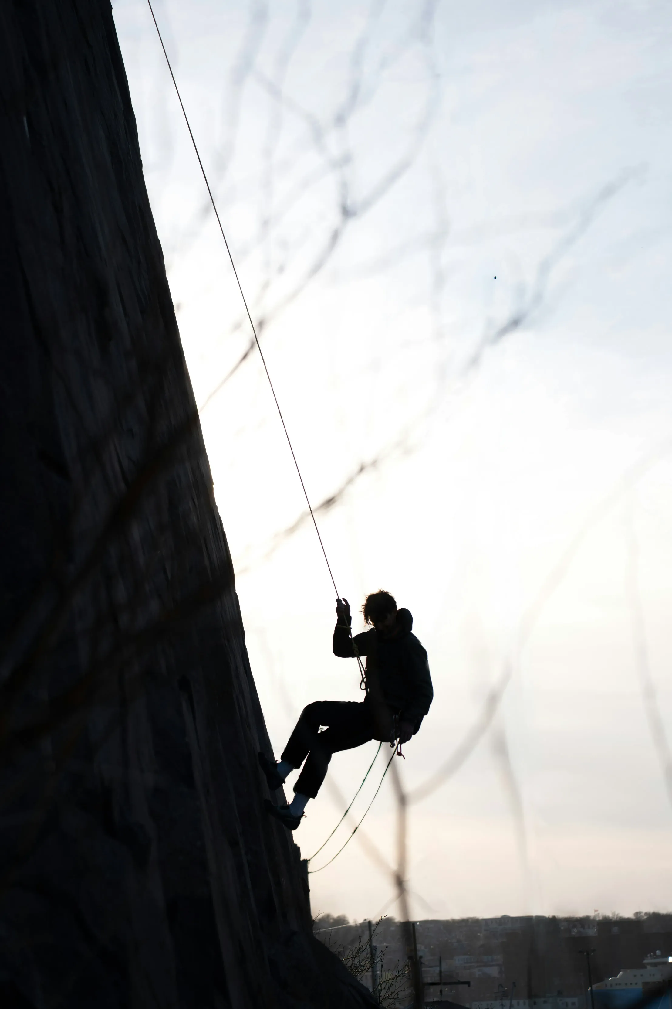 Silhouette of a person rappelling down a rock face.