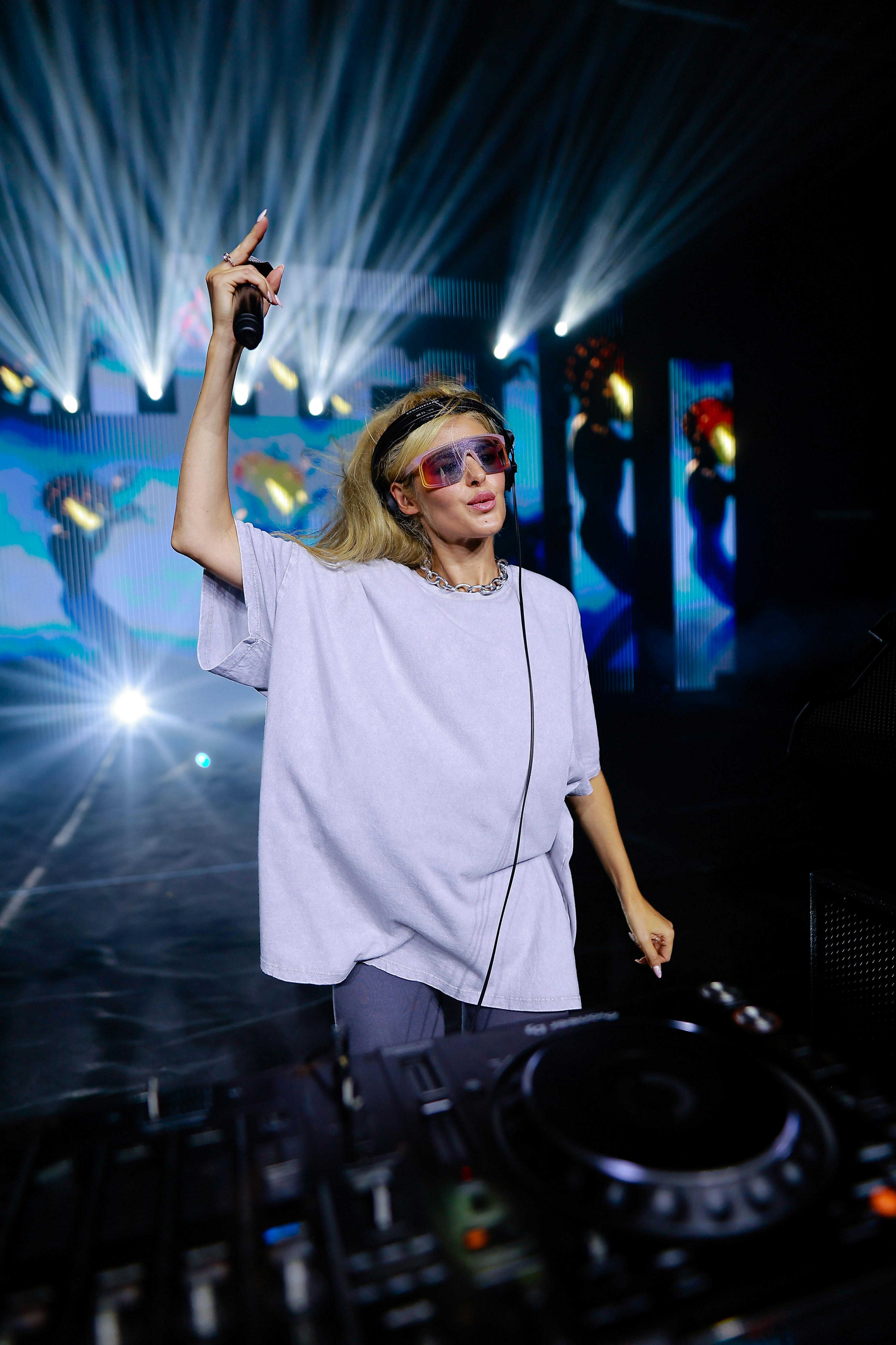 A woman in a white shirt and headphones standing in front of a dj mixer