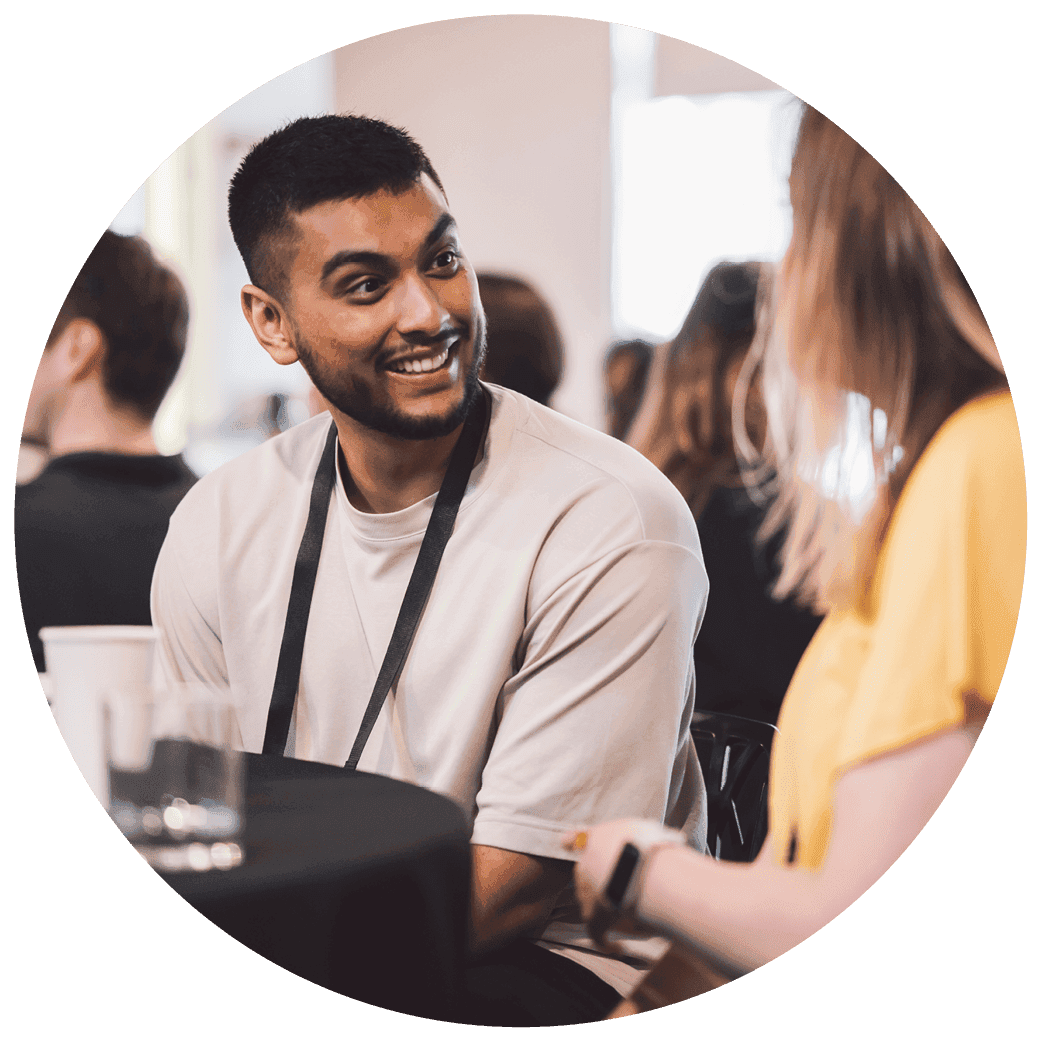 People sitting at a round table during a group conversation in a busy indoor setting.