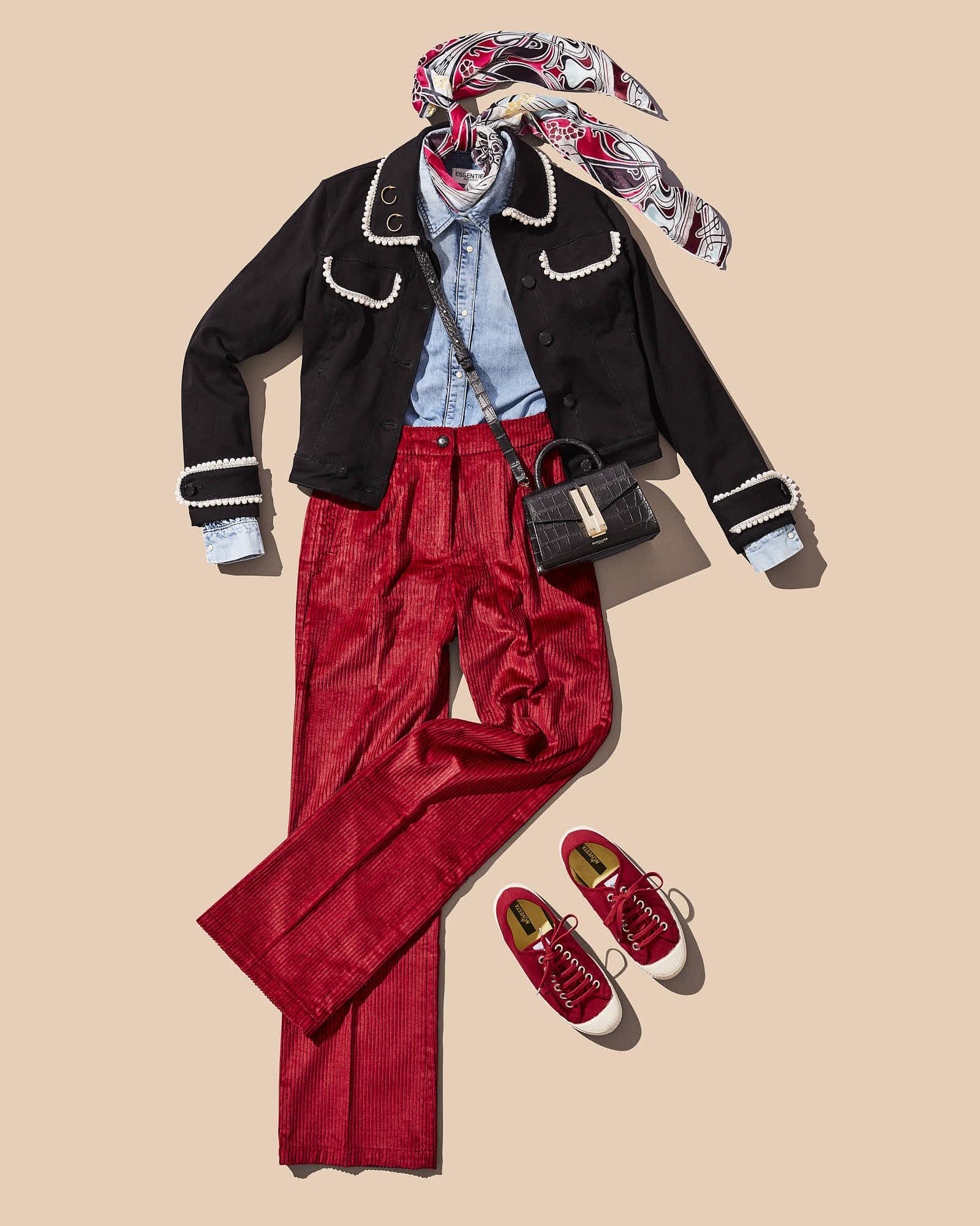 Fashionable outfit with black jacket, red pants, denim shirt, scarf, crossbody bag, and sneakers on beige background.