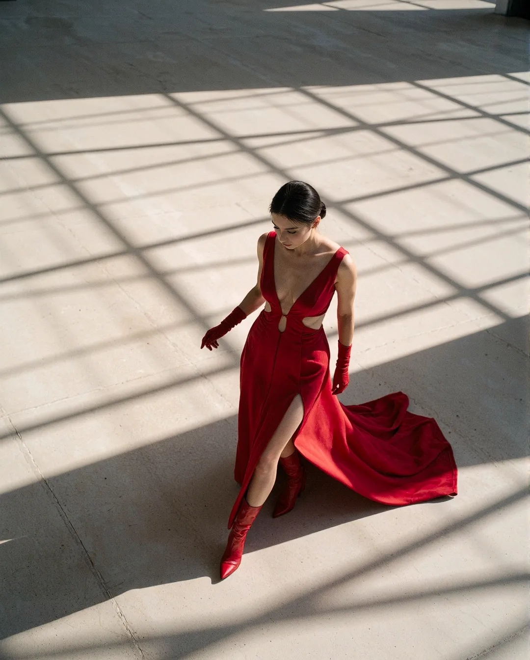Elegant red gown with matching gloves captured in dramatic window light creating geometric shadow patterns on a minimalist floor