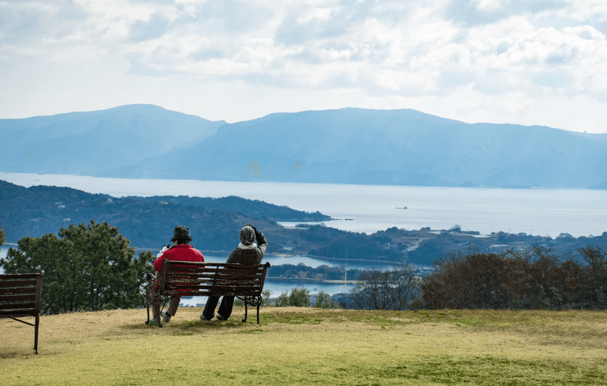 Two older women sitting on a bench in the olive grove, with a stunning view of the Seto sea