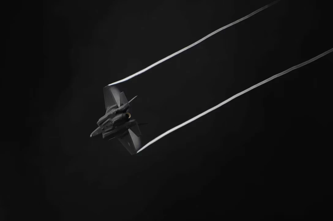 A stealth fighter jet flying with contrails against a dark background.