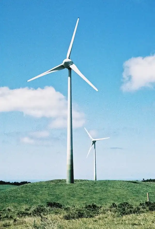 Two white wind turbines on a grassy hill