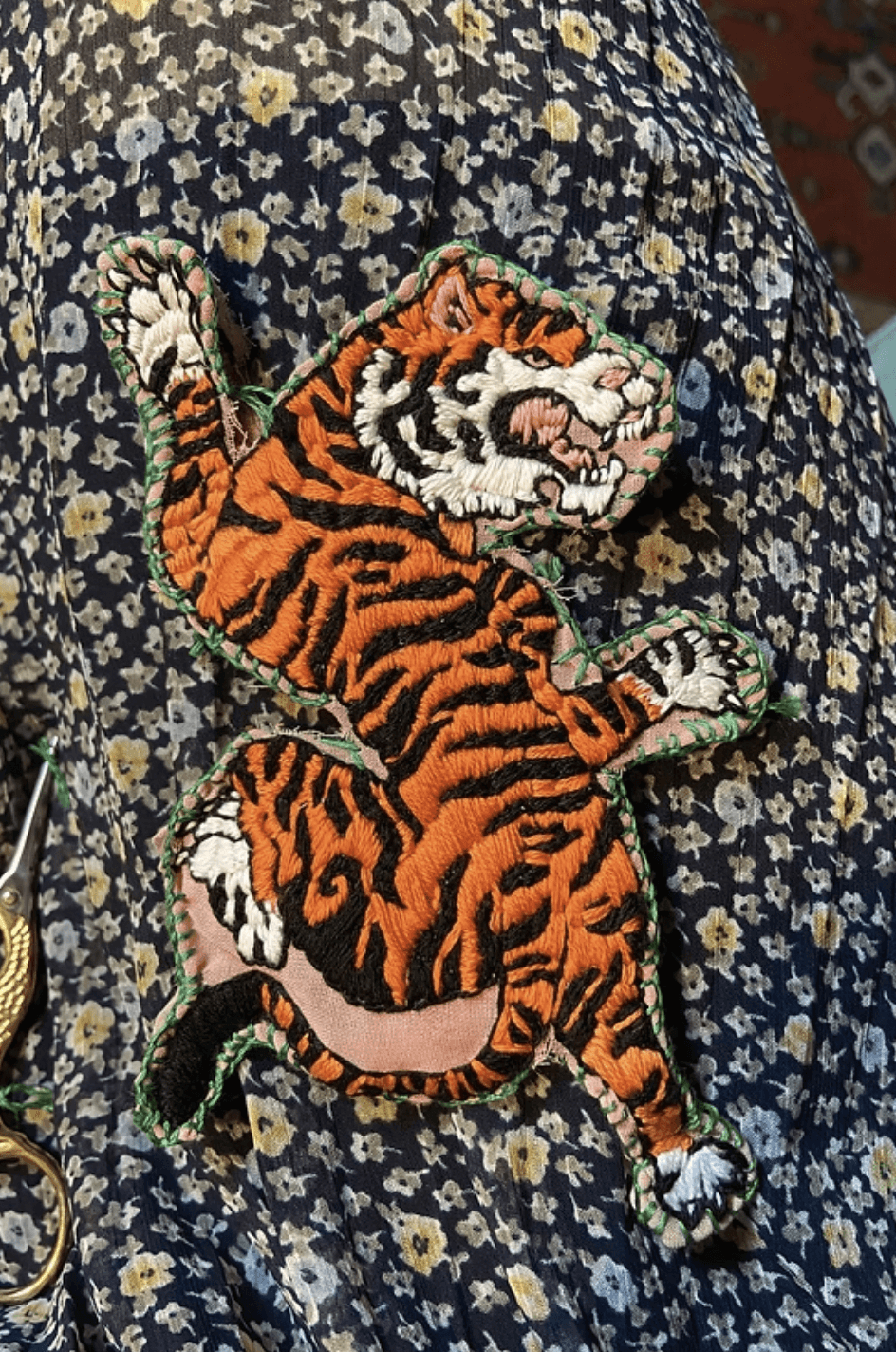 A person stands outdoors in a natural setting with lush green trees under a clear sky, wearing a dark sweatshirt, and looking into the distance.