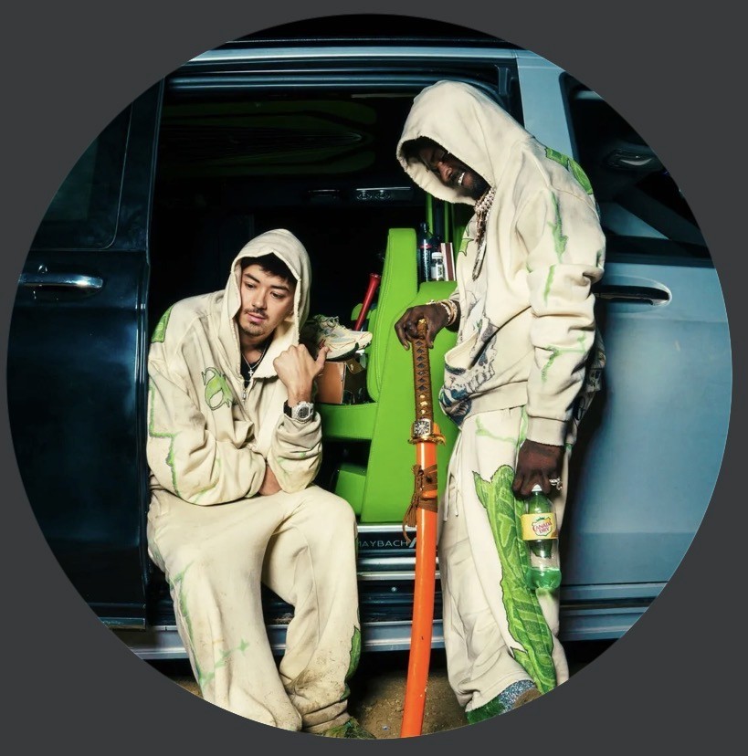 A woman with a red bow headband and bright orange and blue clothing poses against a teal and orange geometric background. Her expression is confident.