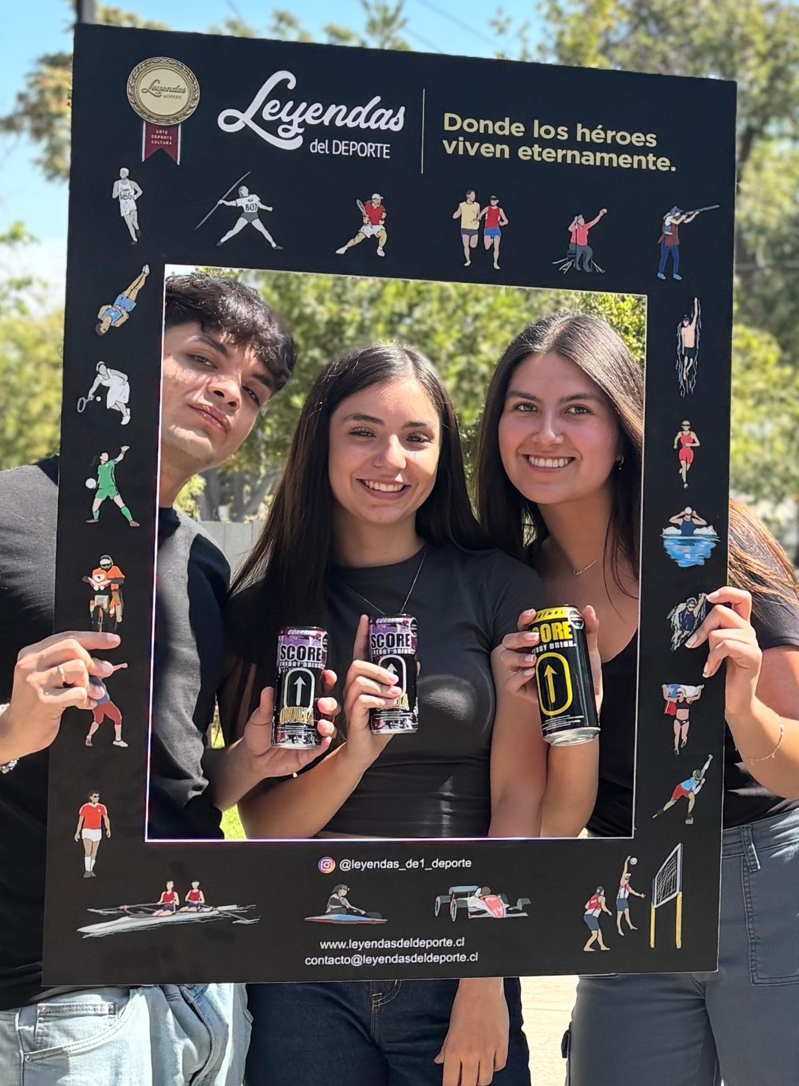 Tres estudiantes con latas de Score energy drink, patrocinador de la exposición Leyendas del Deporte.