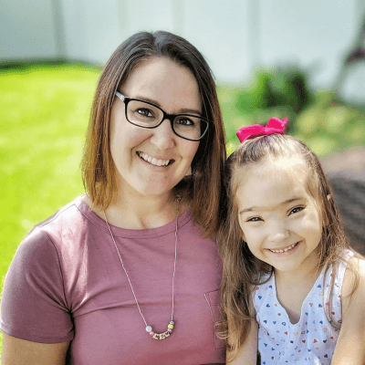 Margaret Block and her daughter sit closely together outdoors, both looking at the camera in a sunny garden setting.