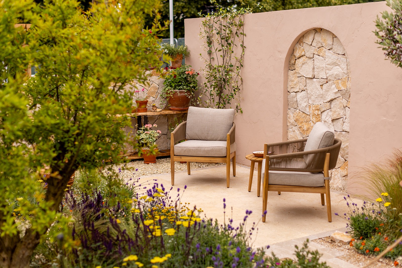 A tranquil outdoor space featuring two wooden chairs and a decorative wall, surrounded by greenery.