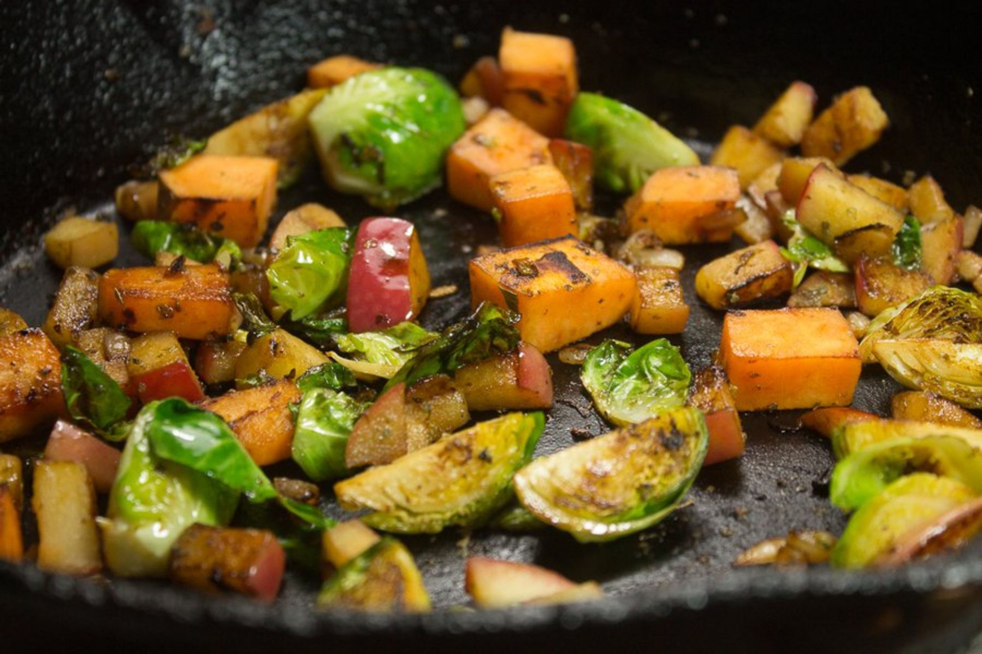 shallots, apples, sweet potatoes, brussels sprouts, and sage being cooked in a pan