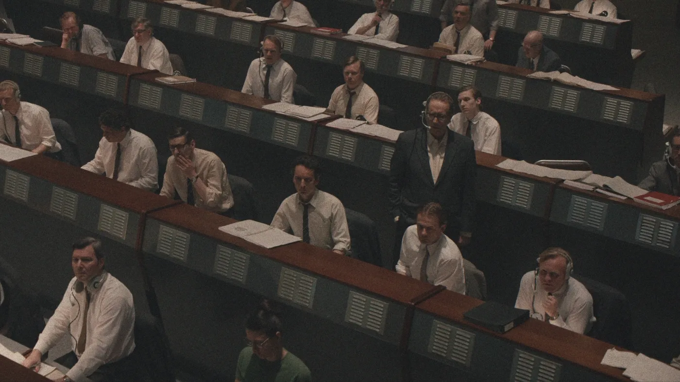 A large group of people, predominantly men in white shirts and ties, are seated and standing in a vintage-style, multi-level mission control room, intently focused on their workstations with large monitors and stacks of paperwork, evoking a historical space operations setting with keywords: mission control, vintage technology, teamwork.