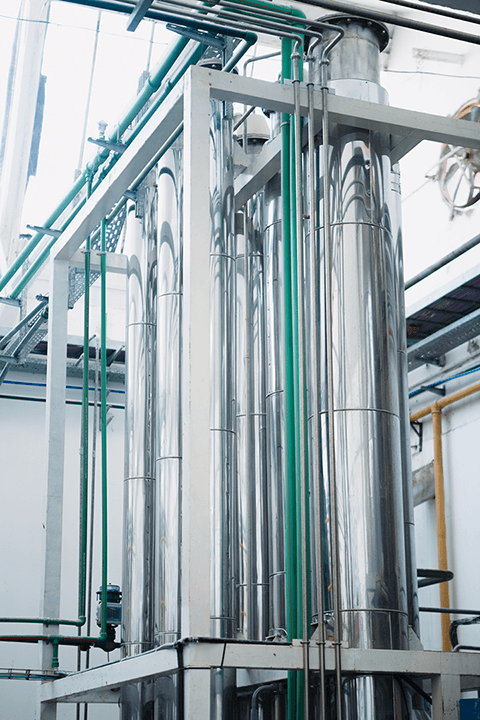 Tall stainless steel processing tanks with connected piping in a manufacturing facility.