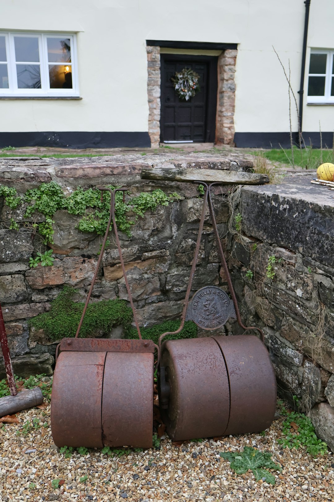 Two rusty antique lawn rollers rest outside.