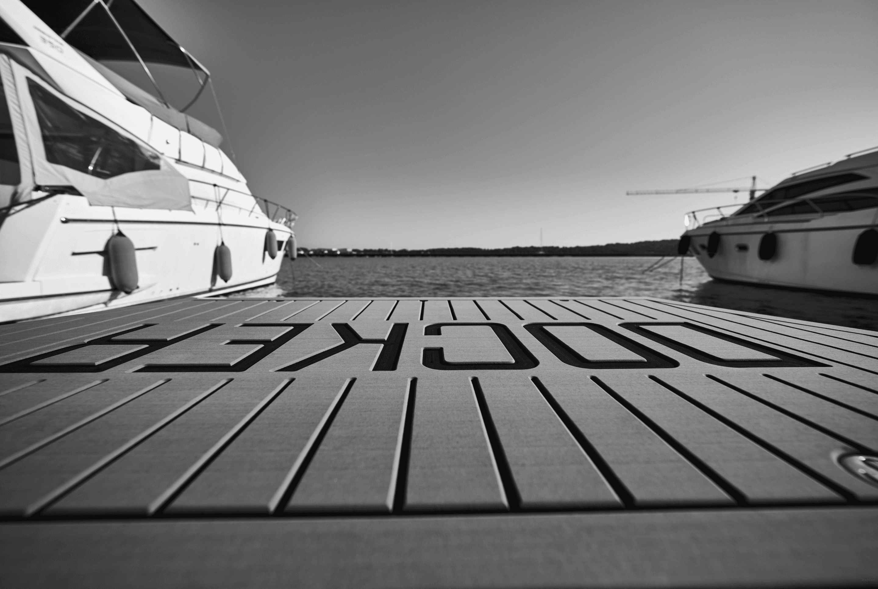 Docker photographed from a dock, some yachts are visible, and a sea is in the distance. The image is in grayscale.