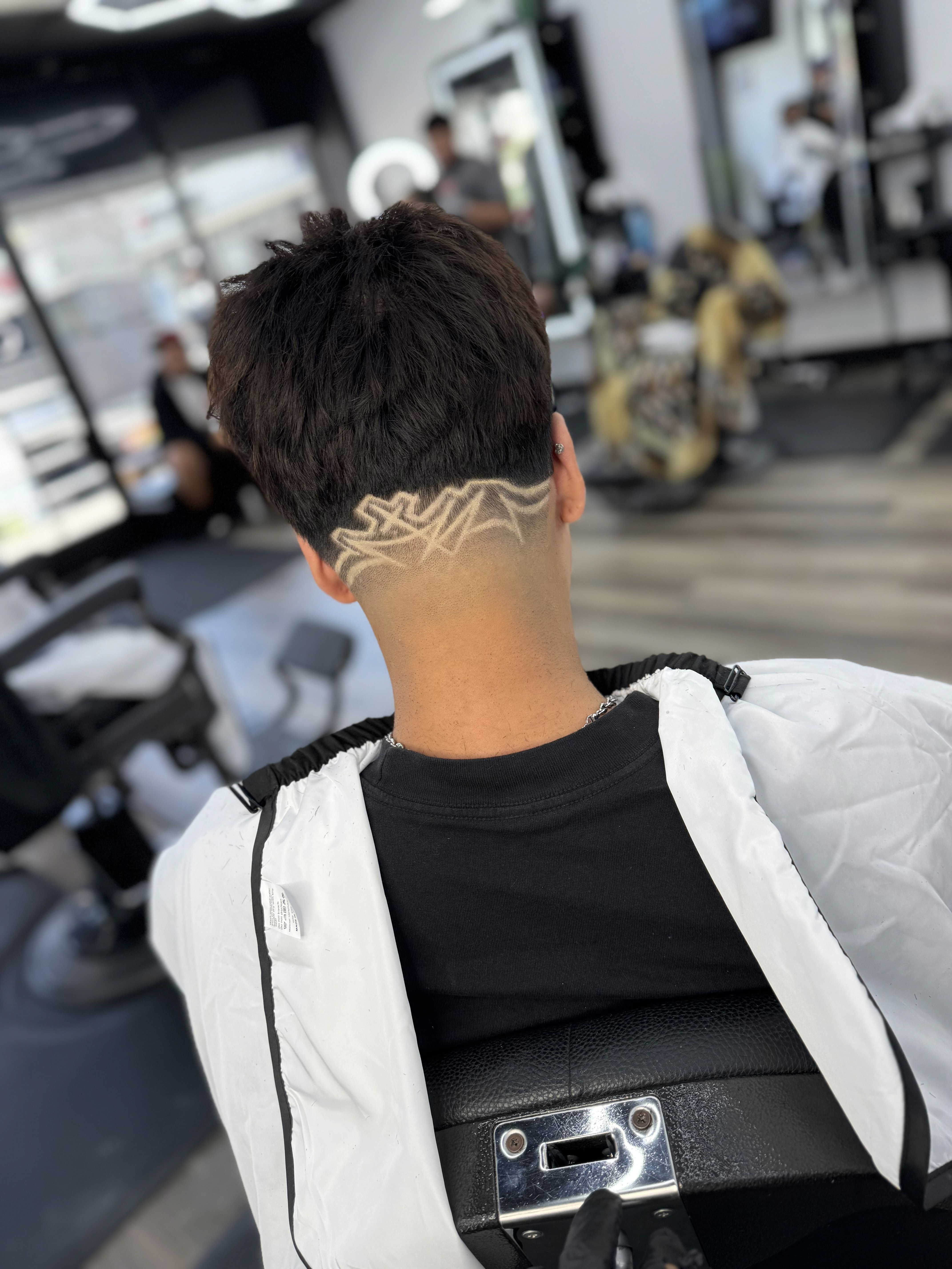 Back view of a man’s haircut featuring a fade with a detailed hair design shaved into the lower section.