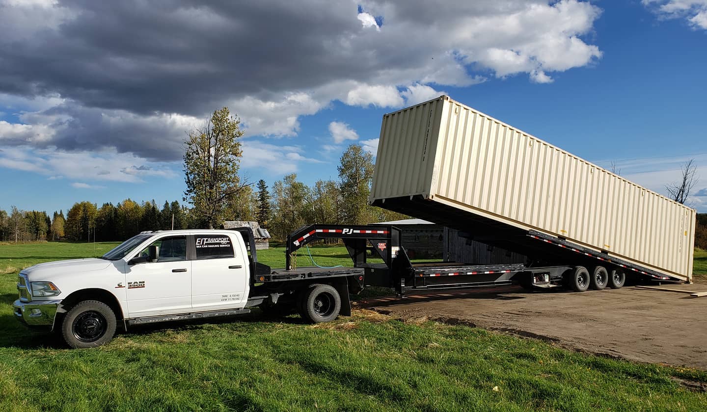 Side view of a new 40-foot high cube beige container being delivered with a tilt deck trailer