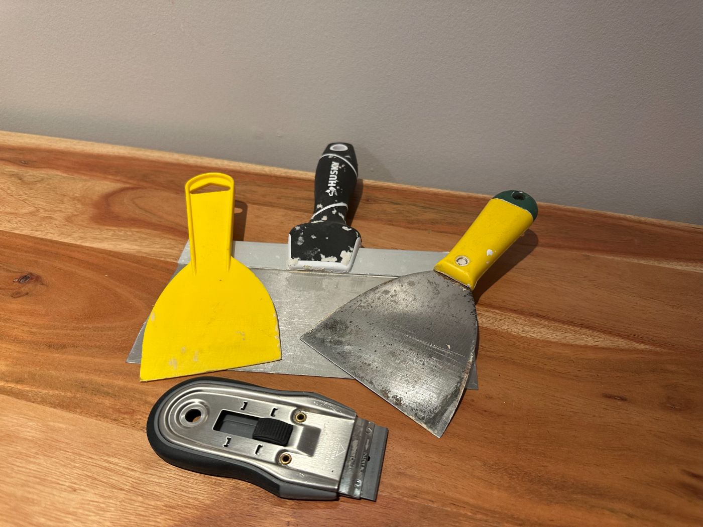 Ensemble de couteaux à mastic et grattoirs Husky pour rénovation, posés sur une table en bois