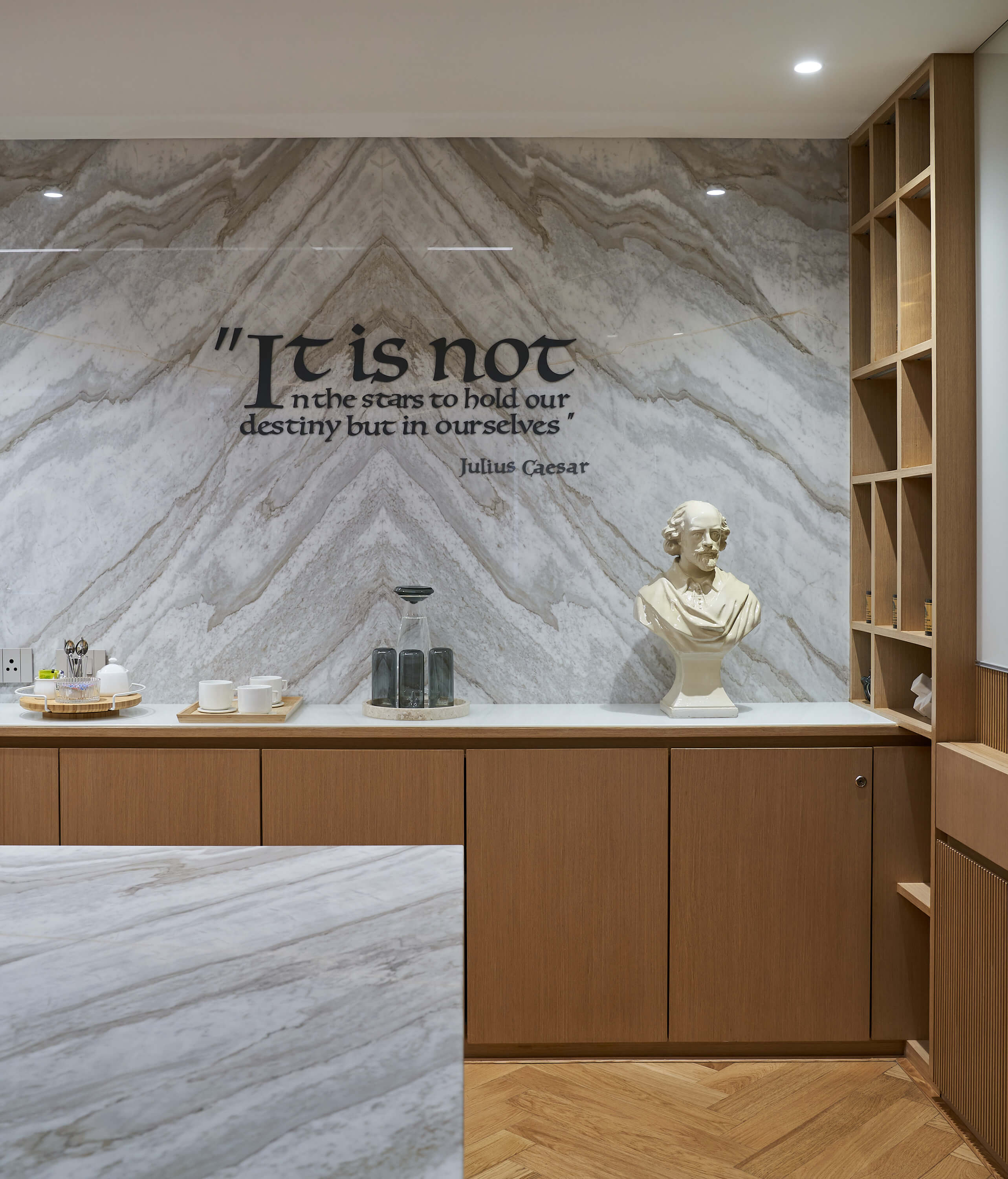 Marble feature wall with Julius Caesar quote above wood credenza and bust sculpture.