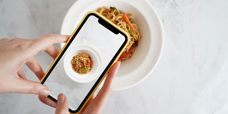 A phone taking a photo of a plate of delicious pasta