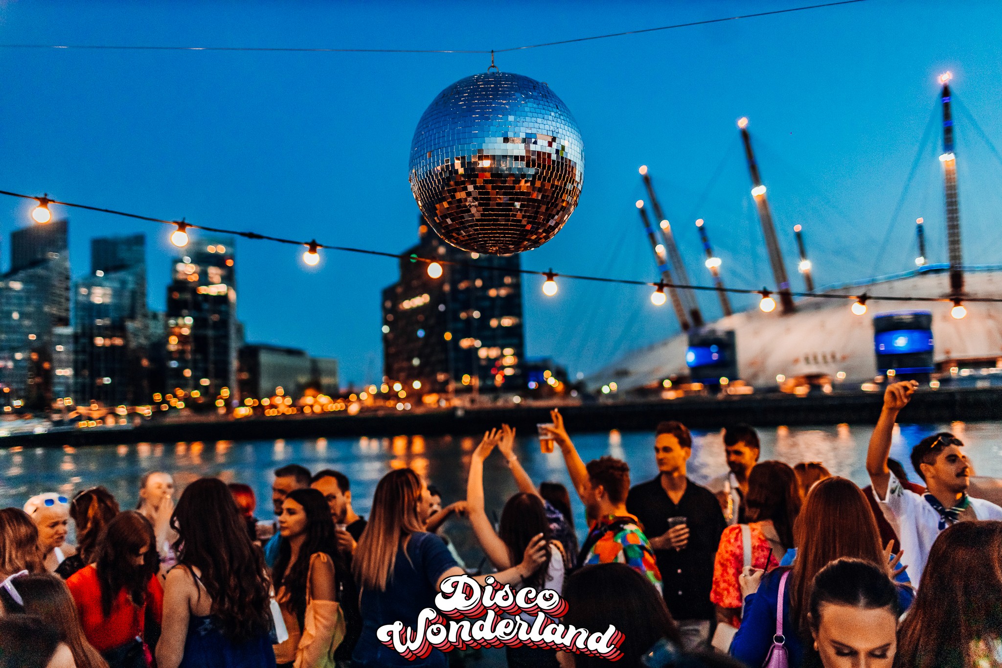 Crowd singing along to ABBA classics on the deck of a London boat party as golden hour turns to dusk