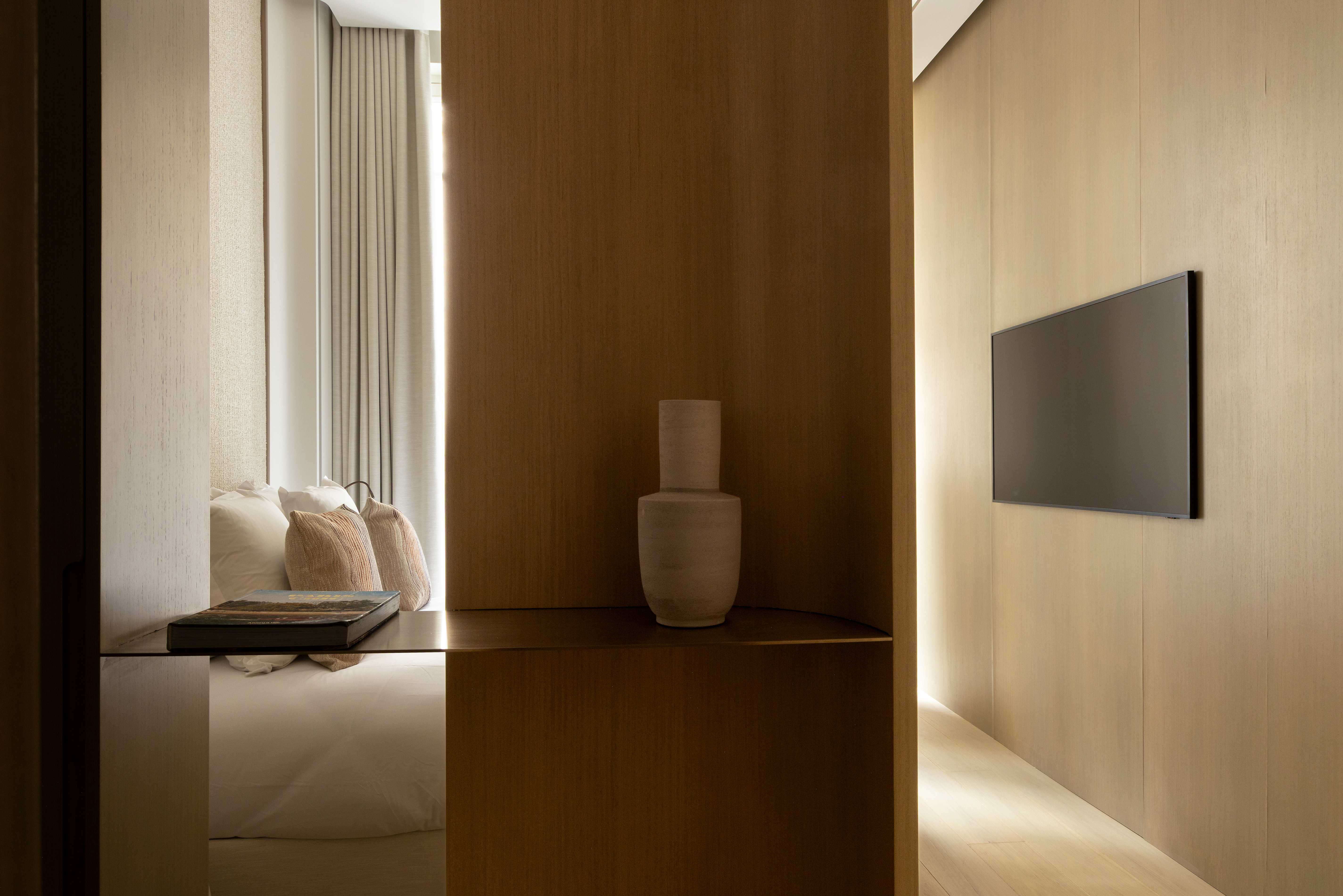 Cloison en bois separant lit et espace television, vase decoratif, livre et eclairage indirect chaleureux
