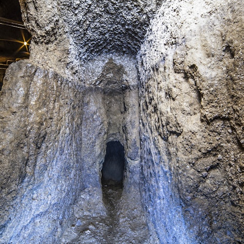 狹窄的石頭隧道，牆壁粗糙且質樸。微弱的燈光照亮了類似洞穴的內部。