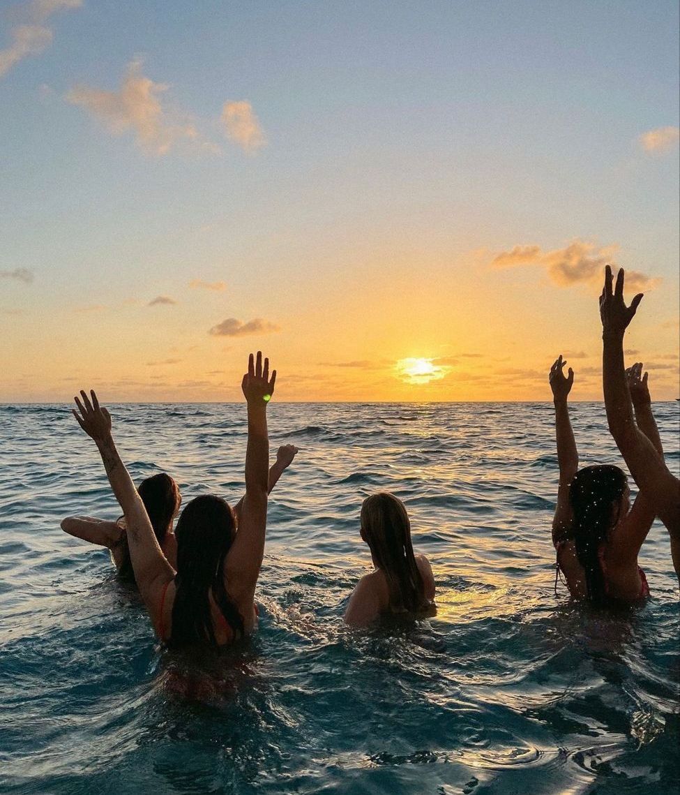 Group of young adults in athletic wear sitting on outdoor steps near a modern overpass, smiling and stretching together in a relaxed, casual moment.