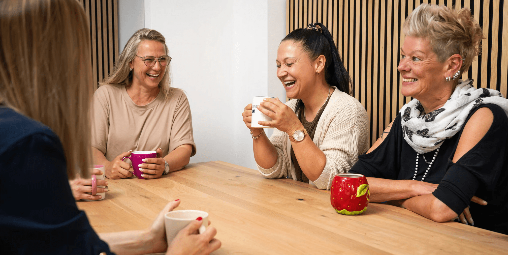 GJP-Mitarbeiterinnen sitzen lachend zusammen an einem Holztisch