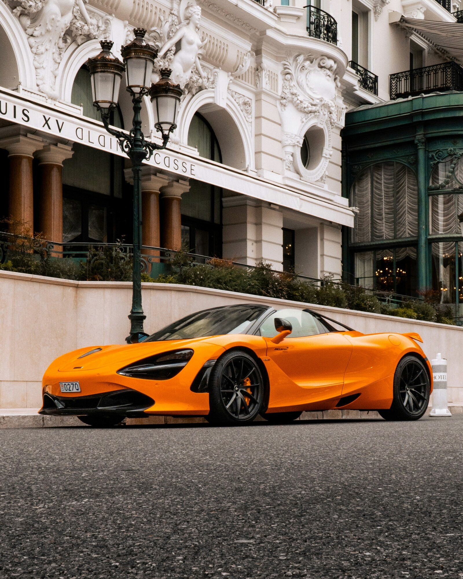 A sleek, bright orange sports car is parked on a city street in front of an ornate, historic building, showcasing its luxury design and modern curves against a classic architectural backdrop.