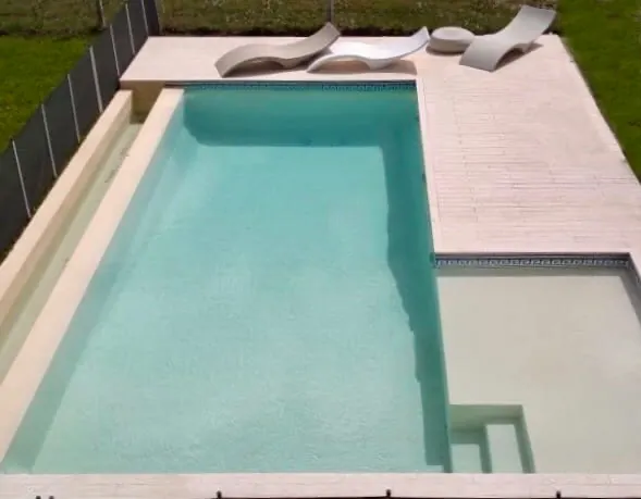 Vista aérea de piscina exterior con amplia escalera interna, revestimiento claro y elegante sector de descanso con reposeras.