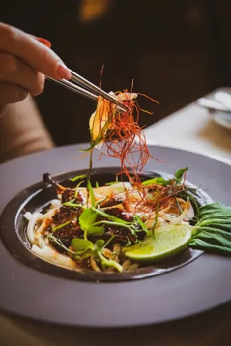 Chef using precision tweezers to add microgreens to a plated dish