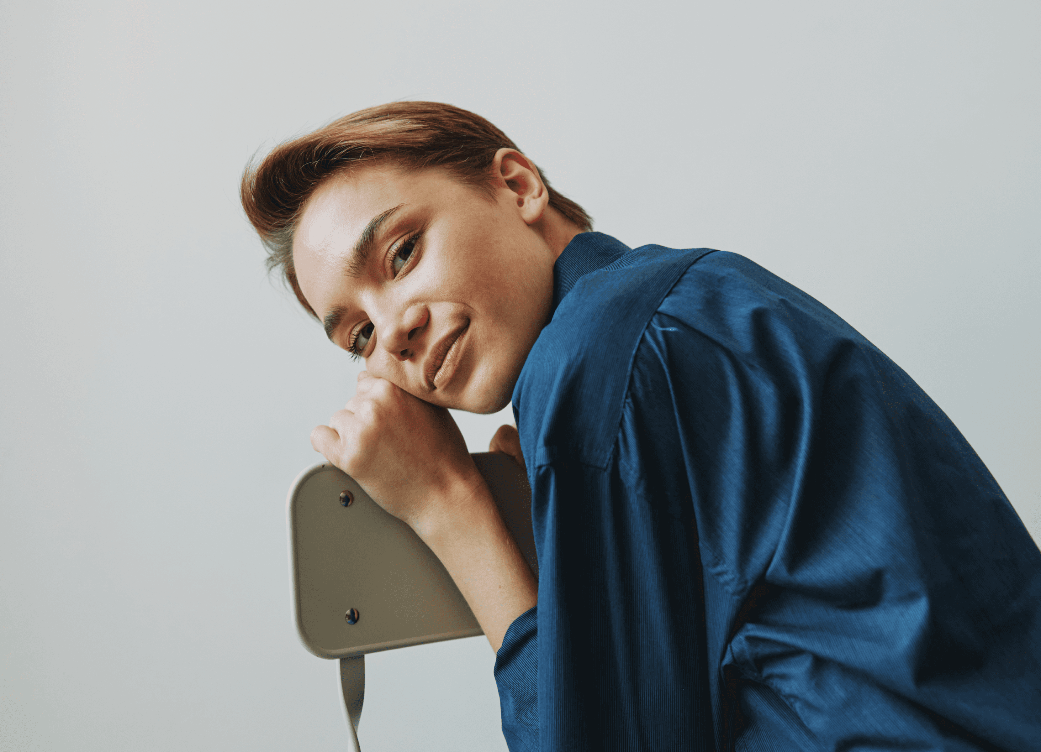 Portrait of young woman leaning on chair in blue shirt, studio shoT.