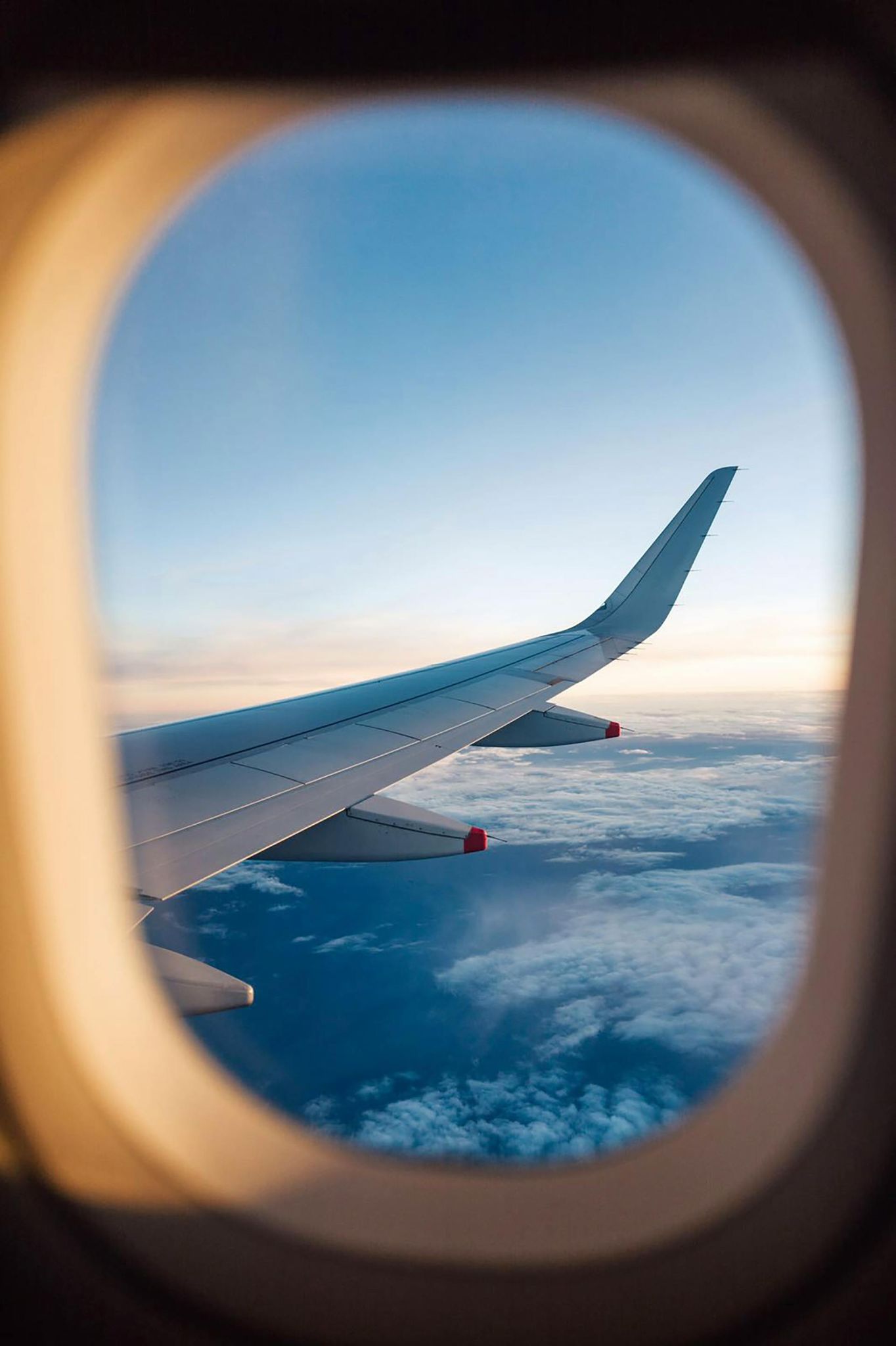 Airplane wing view through window with blue sky and clouds. Travel.