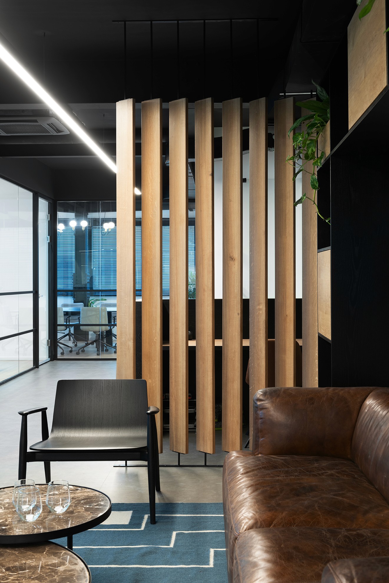 עיצוב משרדים מבוסס מיתוג: דלפק כניסה פיסולי בצורת הלוגו, המשלב צמחייה וניגודיות מול קיר האבן הטבעית